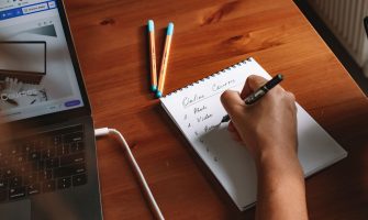 Photo of a person writing a list of online courses on a notepad next to a laptop.