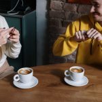 Two individuals communicating using sign language at a cafe table with coffee cups.