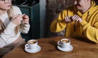 Two individuals communicating using sign language at a cafe table with coffee cups.