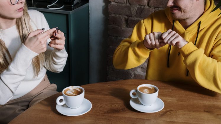 Two individuals communicating using sign language at a cafe table with coffee cups.