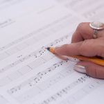 Detailed shot of a hand writing music notes on sheet music, reflecting creativity and composition.