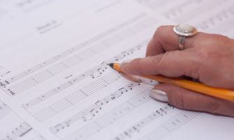 Detailed shot of a hand writing music notes on sheet music, reflecting creativity and composition.