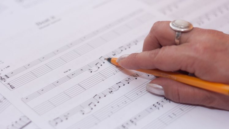 Detailed shot of a hand writing music notes on sheet music, reflecting creativity and composition.
