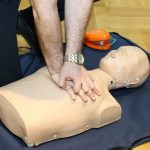 Hands performing CPR on a training dummy using realistic techniques indoors.