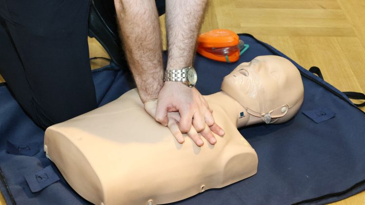Hands performing CPR on a training dummy using realistic techniques indoors.