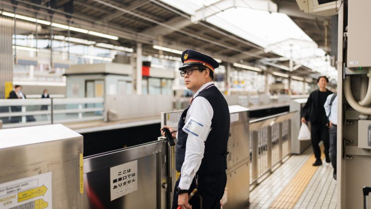 Security guard at a bustling Japanese train station during the day.