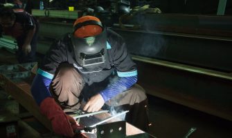 A skilled welder working on metal structures in a Jakarta workshop, showcasing precision and safety protocols.