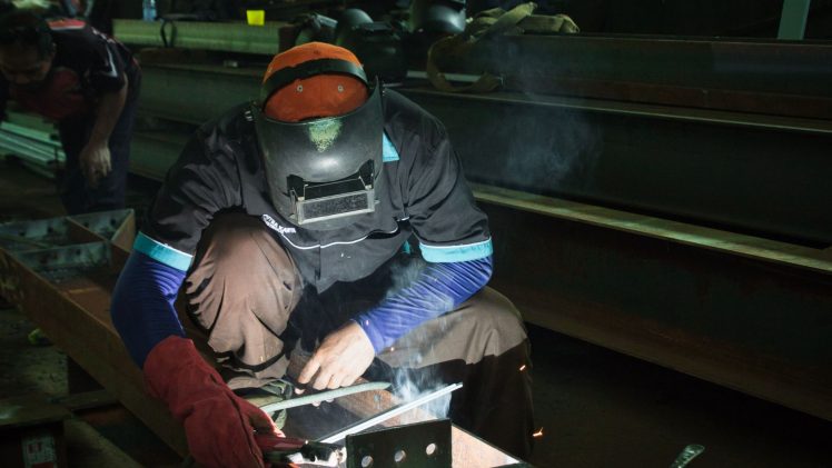 A skilled welder working on metal structures in a Jakarta workshop, showcasing precision and safety protocols.