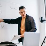 Professional instructor teaching math concepts online with a laptop and whiteboard.