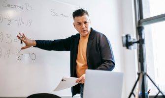 Professional instructor teaching math concepts online with a laptop and whiteboard.