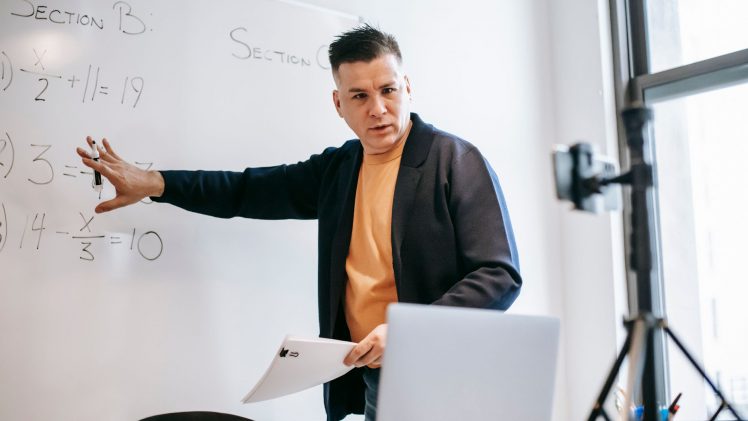 Professional instructor teaching math concepts online with a laptop and whiteboard.
