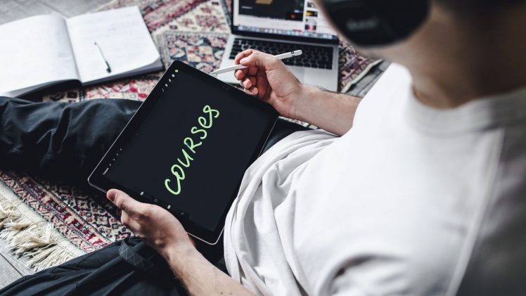 Person studying online courses using a digital tablet while relaxing indoors with headphones.