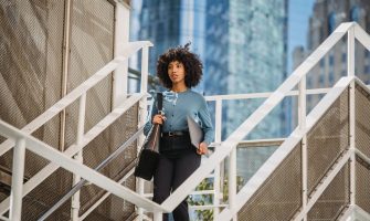 Confident woman carrying a laptop descends stairs in an urban business district.