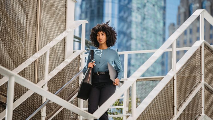 Confident woman carrying a laptop descends stairs in an urban business district.