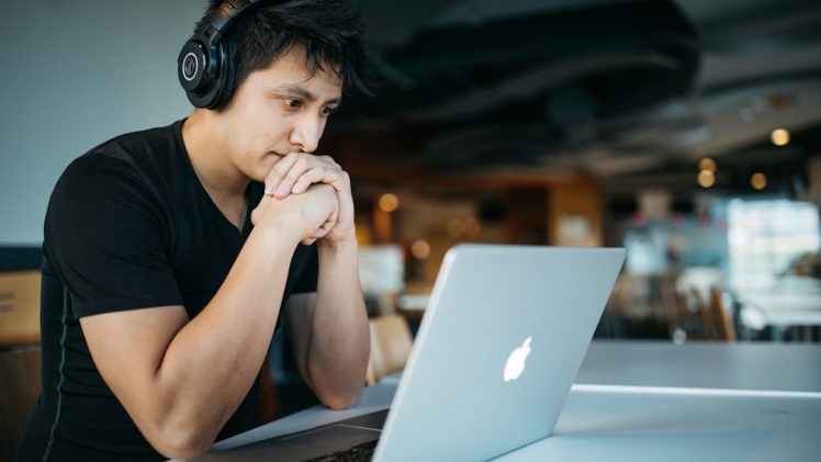 Homem Usando Fones De Ouvido Enquanto Sentado Na Cadeira Em Frente Ao Macbook 4 EeTnaC1S4