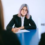 A young woman with dyed hair takes notes during a job interview.