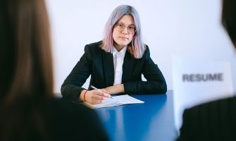A young woman with dyed hair takes notes during a job interview.