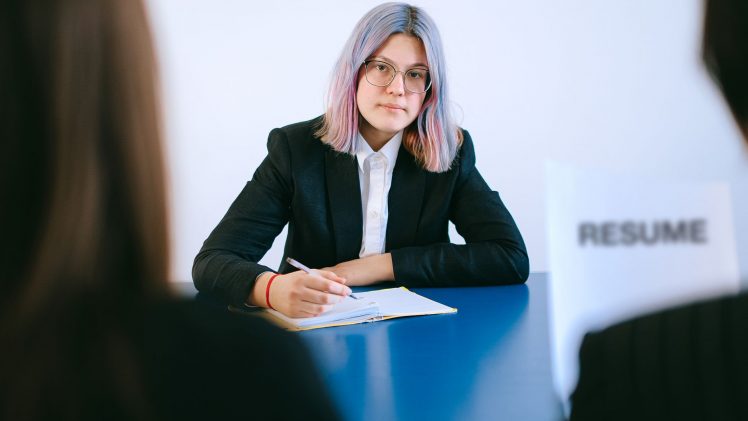 A young woman with dyed hair takes notes during a job interview.
