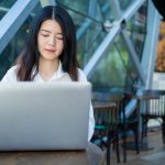 Asian woman working on a laptop in a modern cafe, exemplifying digital entrepreneurship and remote work.