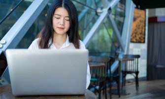 Asian woman working on a laptop in a modern cafe, exemplifying digital entrepreneurship and remote work.