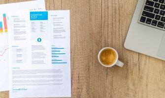 Top view of a desk with resume, coffee cup, and laptop on a wooden surface, ideal for business concepts.