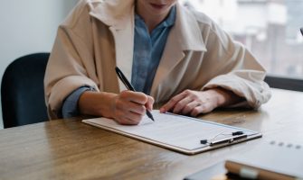 Crop young female unemployed job seeker filling questionnaire sitting at table during interview in office