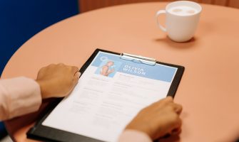 Close-up of hands holding resume during interview with coffee on table, highlighting workplace setting.