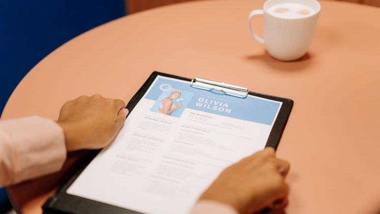 Close-up of hands holding resume during interview with coffee on table, highlighting workplace setting.