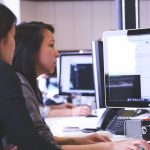 Two women working together on code at a computer in a modern office setting.