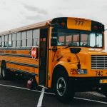 Classic American yellow school bus parked by a serene lakeside in an urban setting.