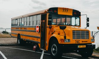 Classic American yellow school bus parked by a serene lakeside in an urban setting.