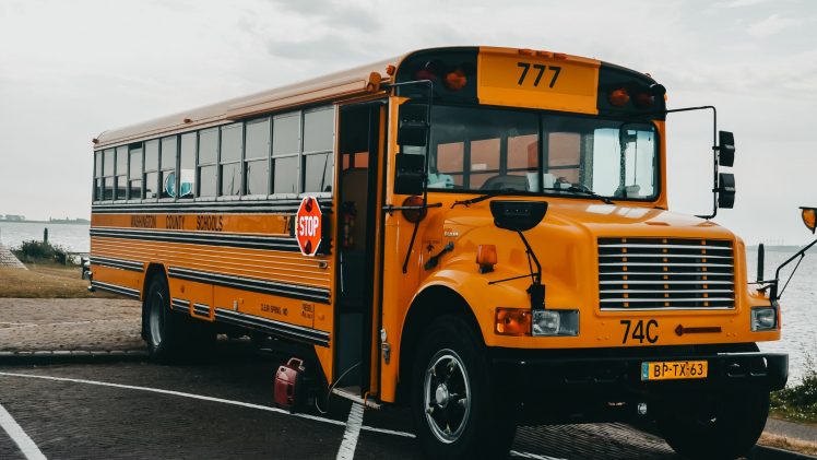Classic American yellow school bus parked by a serene lakeside in an urban setting.
