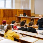 Students engaging with a professor in a university lecture hall, utilizing technology.
