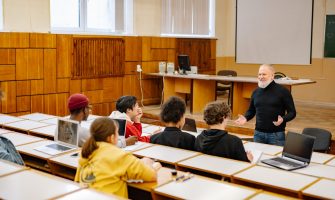 Students engaging with a professor in a university lecture hall, utilizing technology.
