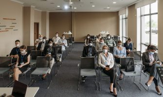 Attendees wearing masks in a socially distanced setup during a business meeting to ensure safety.