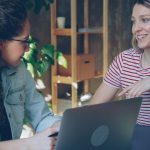 Two women engaged in a friendly business meeting indoors with a laptop.