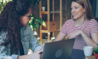 Two women engaged in a friendly business meeting indoors with a laptop.