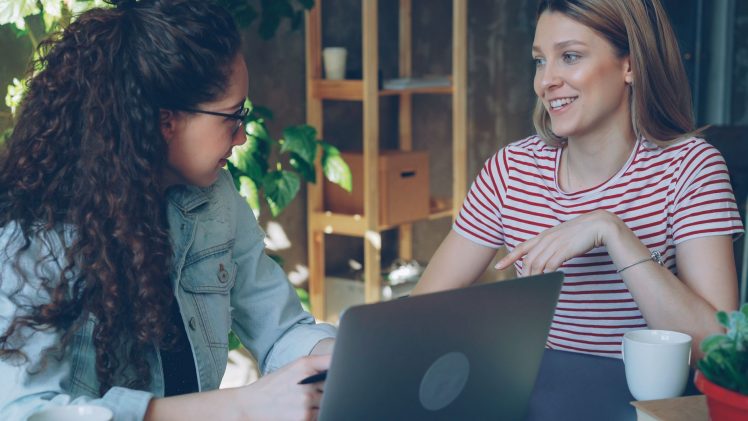 Two women engaged in a friendly business meeting indoors with a laptop.