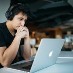 Homem Usando Fones De Ouvido Enquanto Sentado Na Cadeira Em Frente Ao Macbook 4 EeTnaC1S4