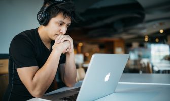 Homem Usando Fones De Ouvido Enquanto Sentado Na Cadeira Em Frente Ao Macbook 4 EeTnaC1S4