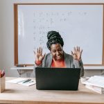 Cheerful African American female teaching online lesson with netbook in modern classroom