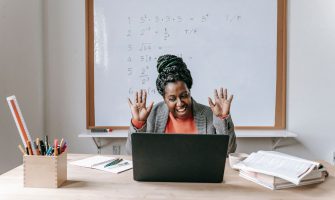 Cheerful African American female teaching online lesson with netbook in modern classroom