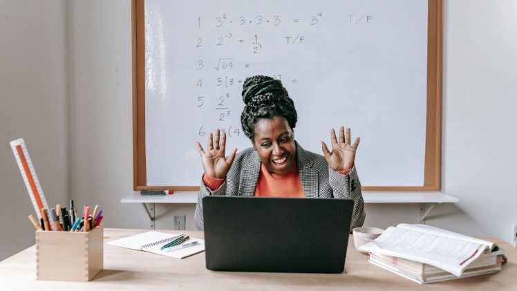 Cheerful African American female teaching online lesson with netbook in modern classroom