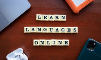 Flat lay of language learning tools with devices and text blocks on desk.