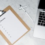 A clipboard with a resume beside a pen and laptop on a marble desk, ideal for business and job application themes.