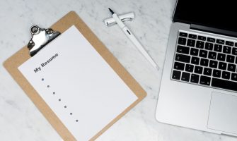 A clipboard with a resume beside a pen and laptop on a marble desk, ideal for business and job application themes.