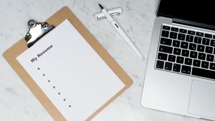 A clipboard with a resume beside a pen and laptop on a marble desk, ideal for business and job application themes.