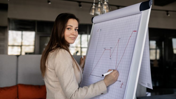 Confident woman illustrating sales growth on a flipchart in a modern office.