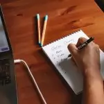 Photo of a person writing a list of online courses on a notepad next to a laptop.
