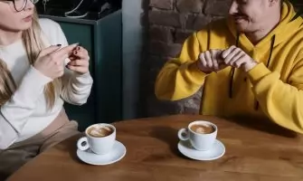 Two individuals communicating using sign language at a cafe table with coffee cups.